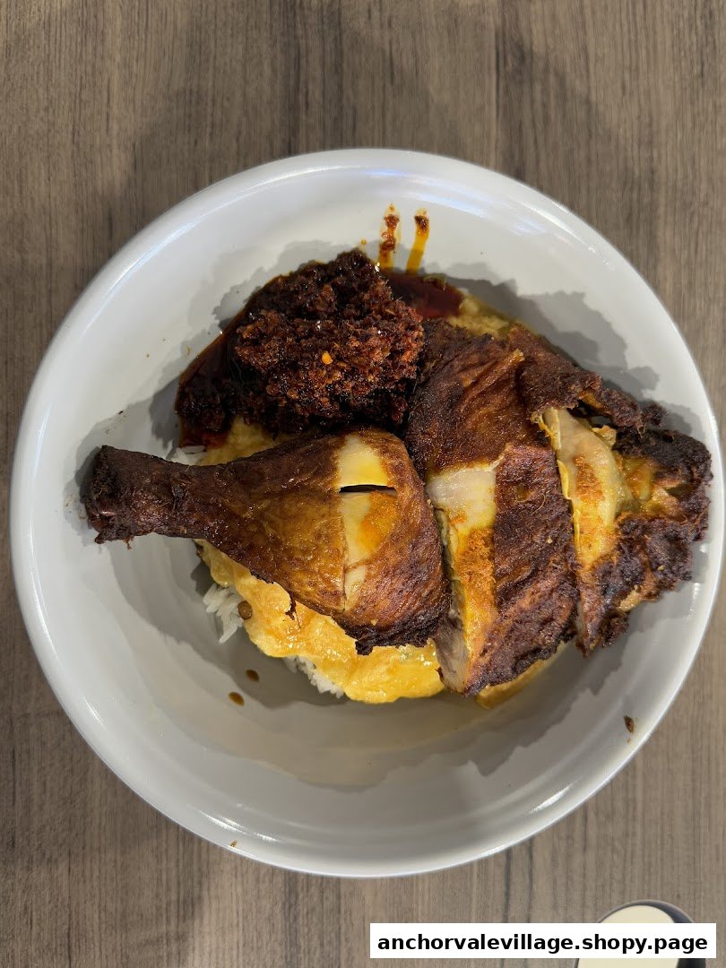 A close-up of a delicious roasted chicken dish with rice and sambal in a white bowl.