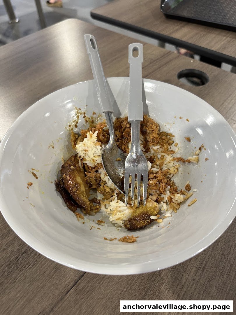 A close-up of a partially eaten meal with rice, meat, and sauce in a white bowl.