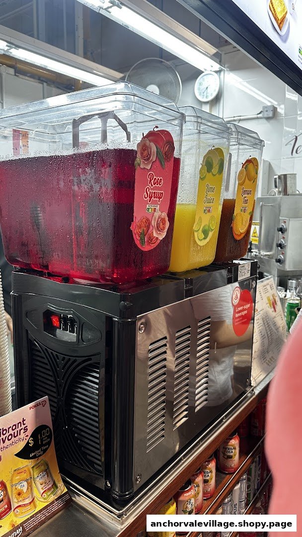 A beverage dispenser at Kopi Kiosk offering Rose Syrup, Lime Juice, and Lemon Tea, with canned drinks below.