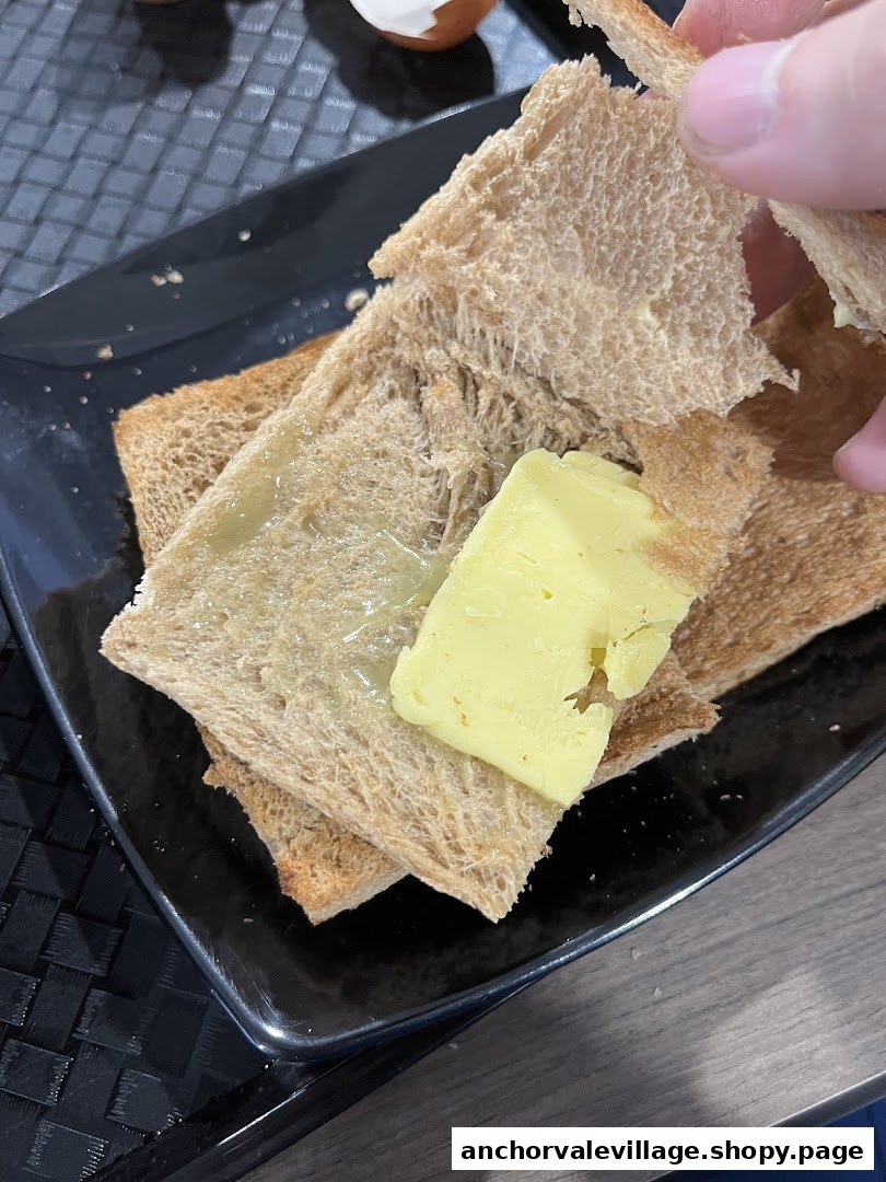 A close-up of traditional kaya butter toast on a black plate, with a hand holding a piece.