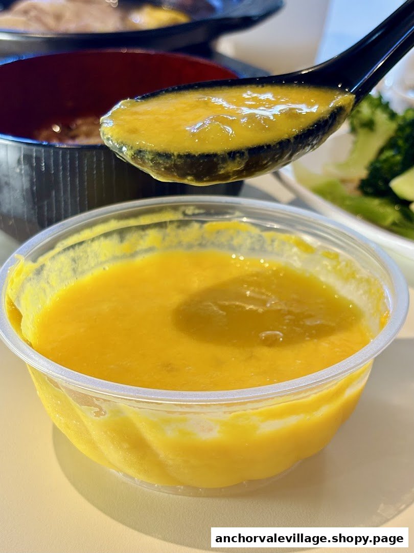 A close-up of a rich, golden-yellow soup or dessert in a clear bowl, with a spoonful lifted.