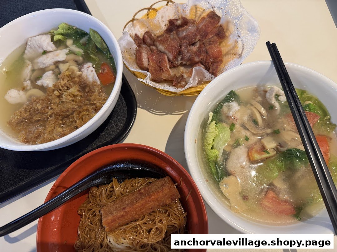 A table with two bowls of fish soup, dry noodles, and a side of fried meat.