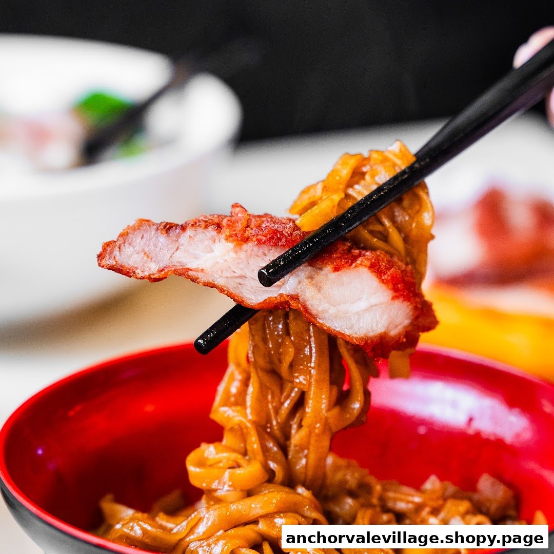 Chopsticks lift savory noodles and crispy fried pork from a vibrant red bowl.