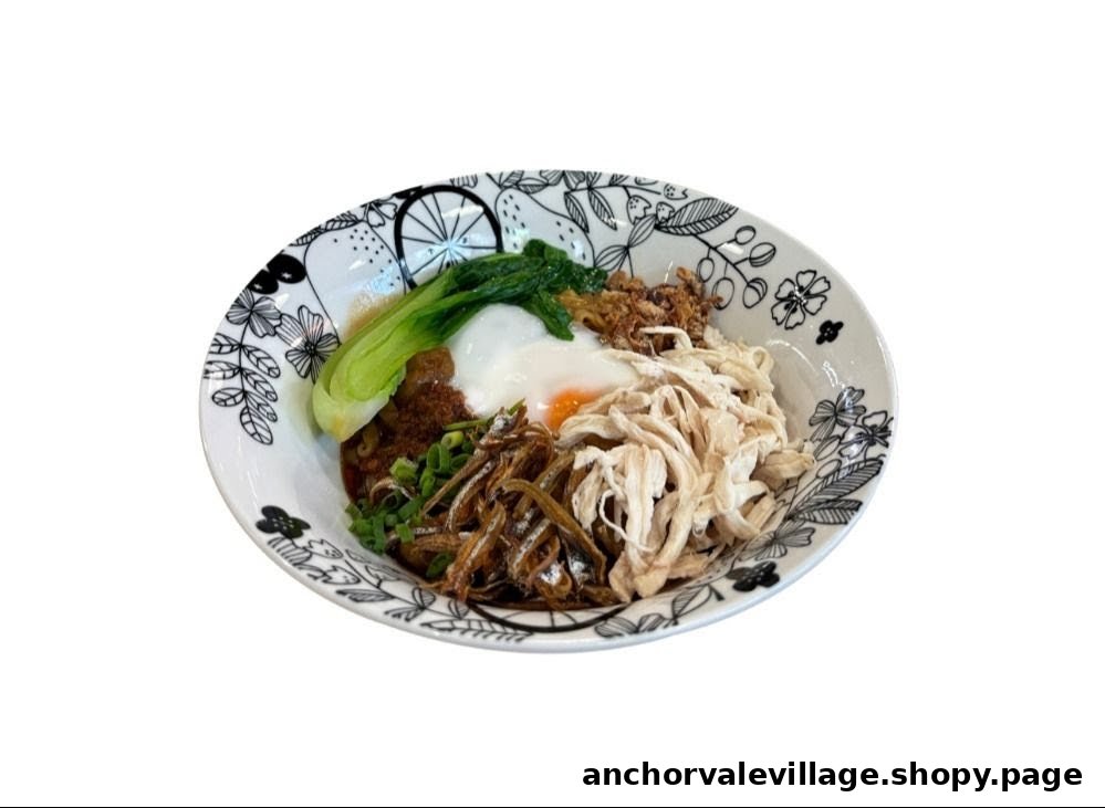 A vibrant bowl of noodles topped with shredded chicken, crispy anchovies, a poached egg, and greens.
