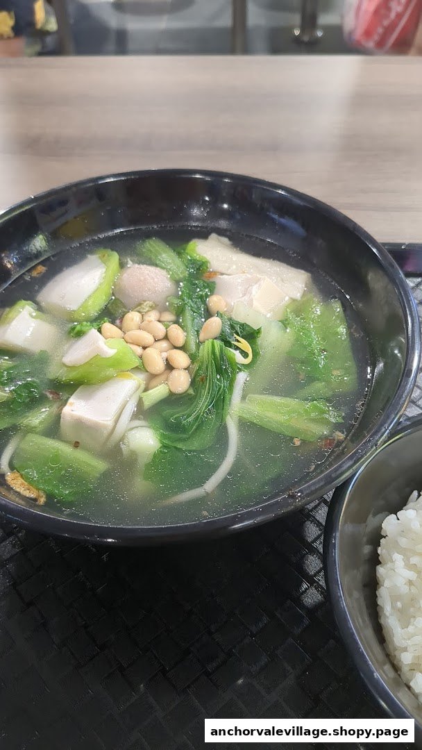 A close-up of a bowl of Yong Tau Foo soup with various ingredients and a side of rice.
