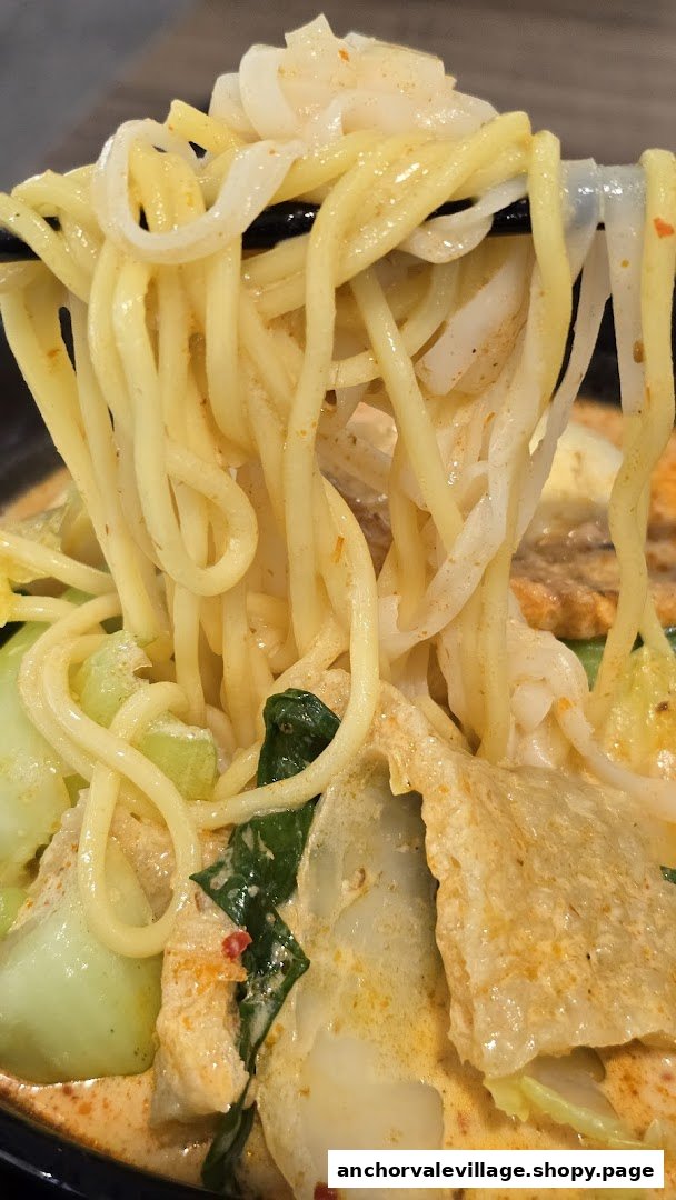 Close-up of chopsticks lifting noodles and ingredients from a bowl of Yong Tau Foo.