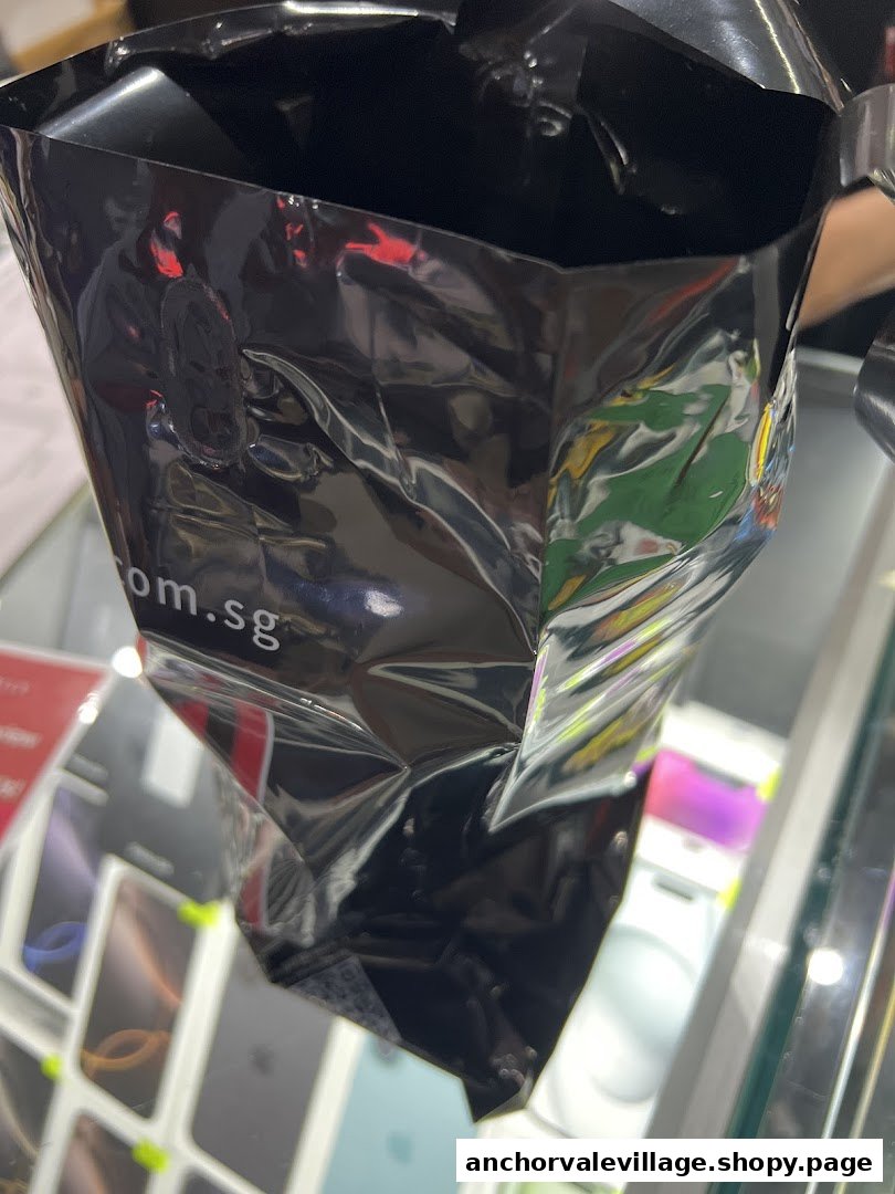 Close-up of a black reflective bag, possibly product packaging, with mobile phones visible in the background.
