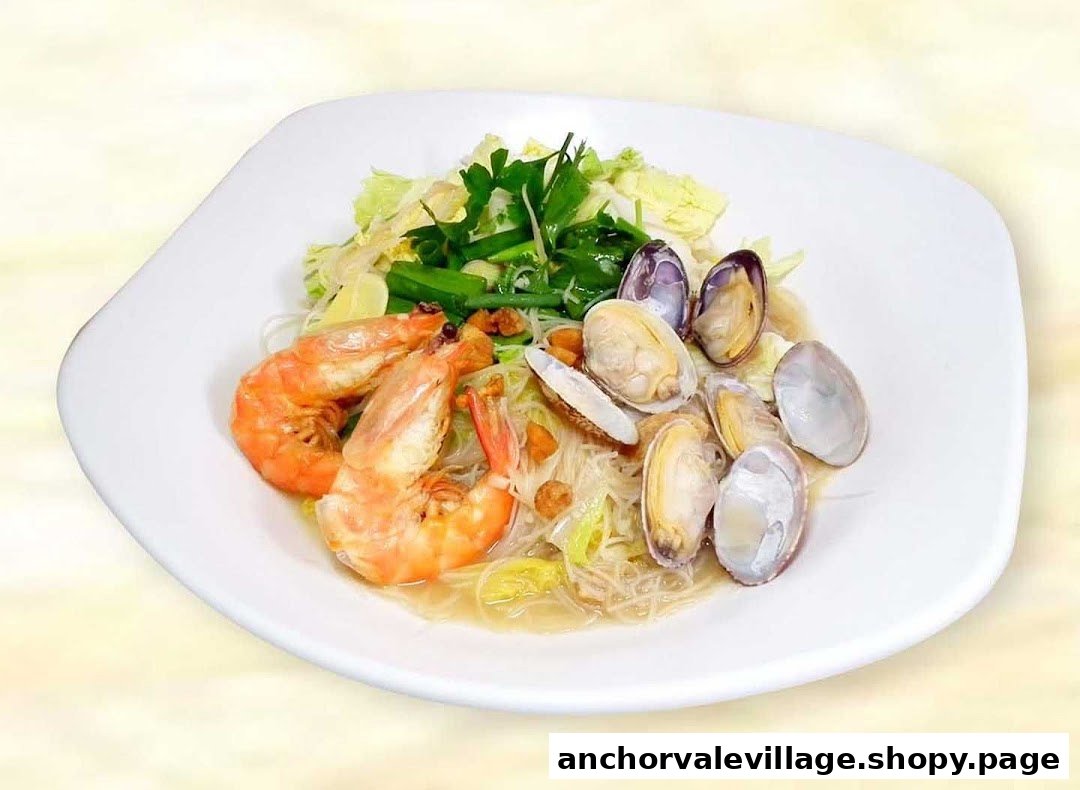 A white plate features a delicious seafood noodle dish with large prawns, clams, and fresh vegetables.