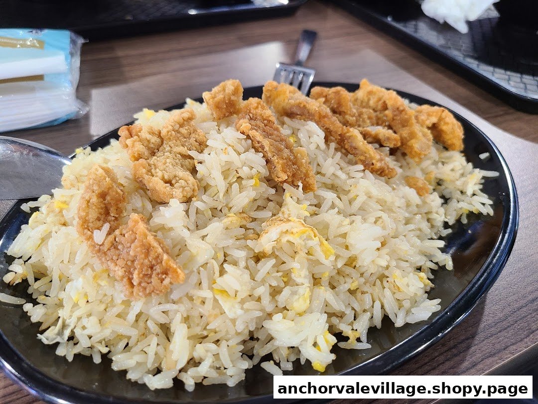 A close-up of a plate of fried rice topped with crispy golden fried chicken or fish pieces.