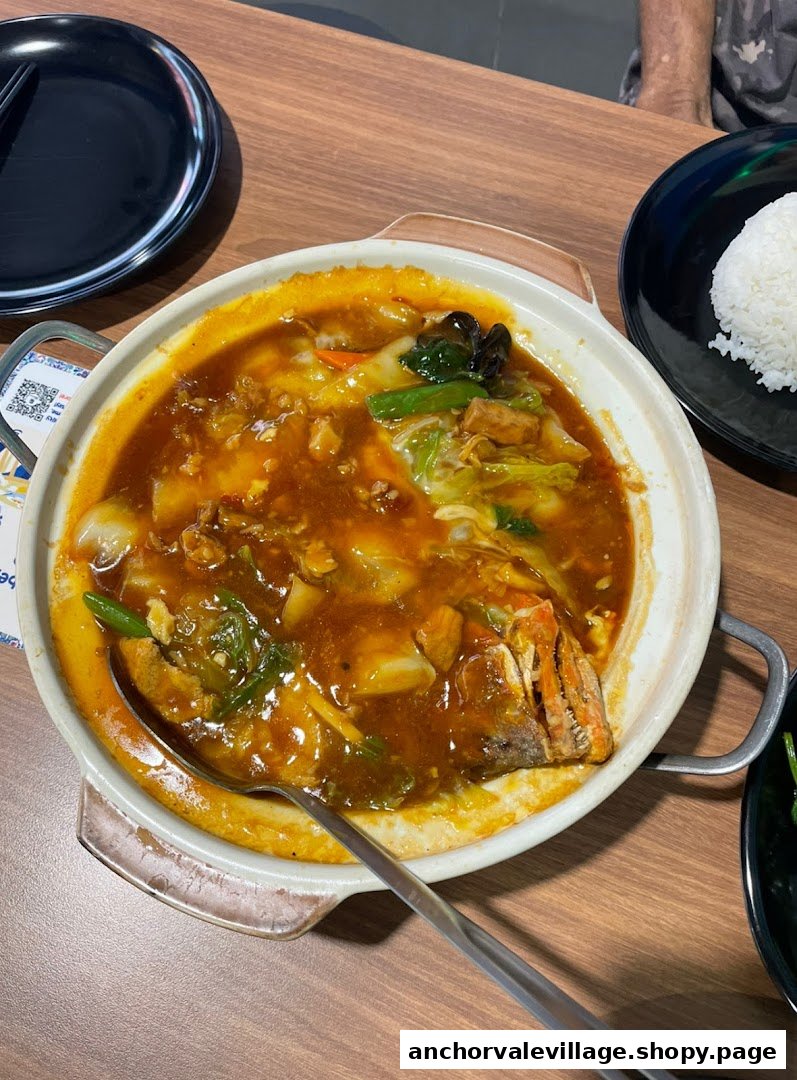 A large claypot of braised fish head with vegetables and sauce, served with rice.