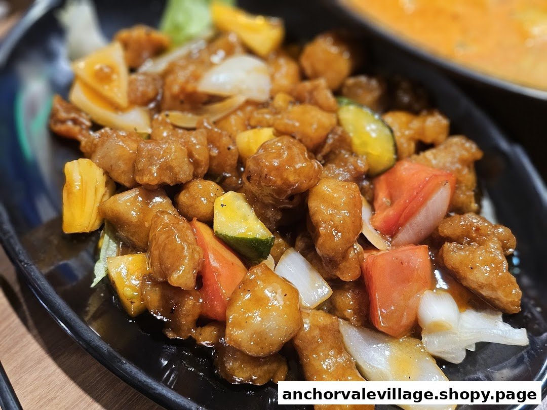 A close-up of a delicious sweet and sour dish with meat, pineapple, and vegetables on a black plate.