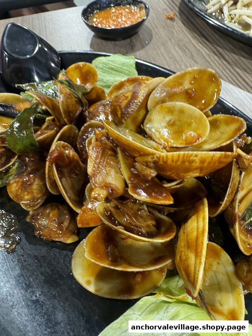 A close-up of a delicious plate of stir-fried clams with sauce and herbs.