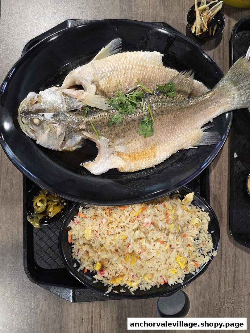 A delicious steamed fish with cilantro and a side of flavorful fried rice on a black tray.