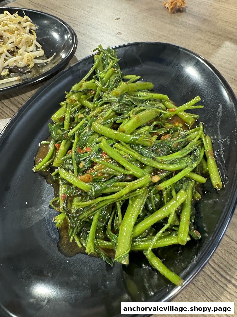 A vibrant plate of stir-fried water spinach with garlic and chili, with bean sprouts in background.
