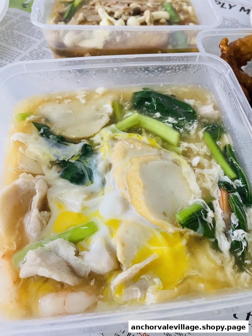 A close-up of a saucy seafood and noodle dish with egg, vegetables, and meat in a clear takeaway container.
