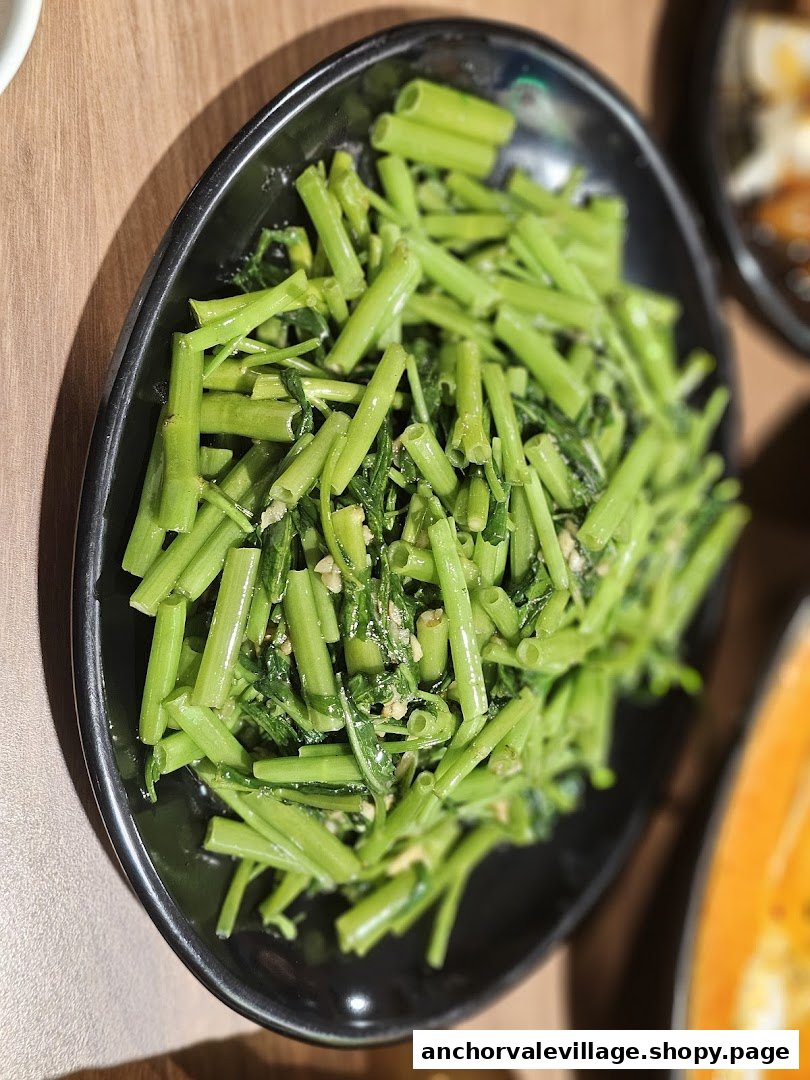 A close-up of a vibrant green stir-fried vegetable dish, likely water spinach, served on a black plate.