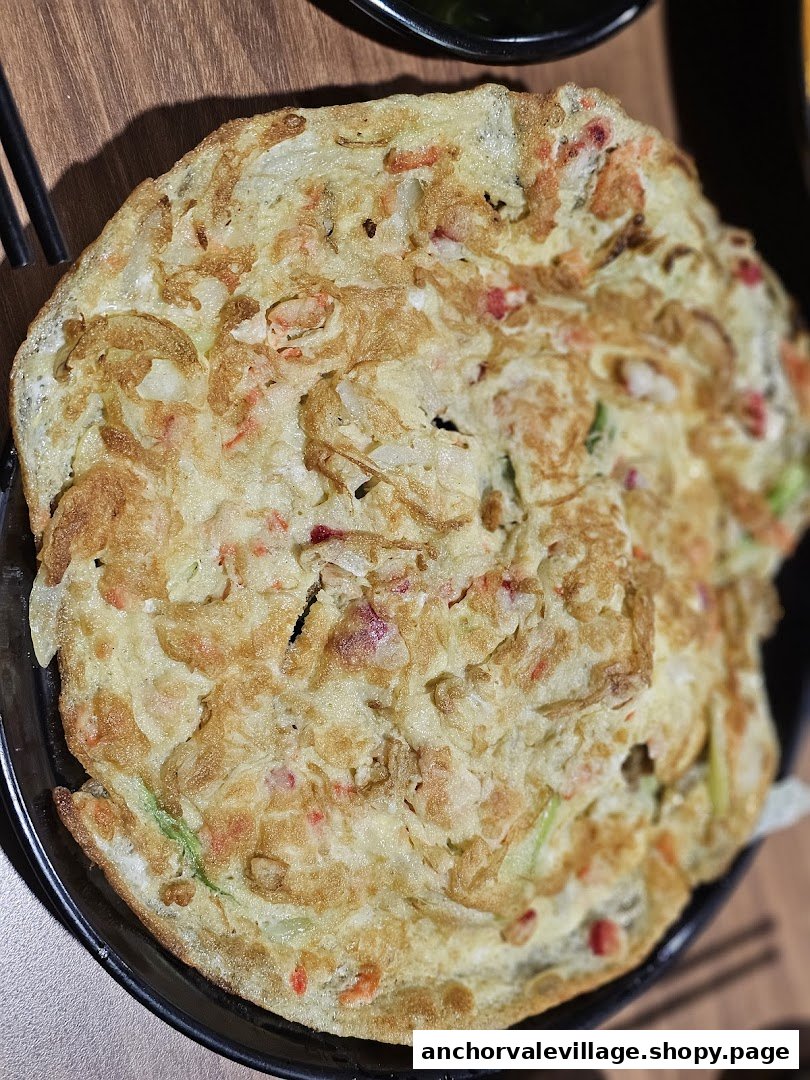 A close-up of a golden-brown seafood pancake or omelet, rich with various ingredients.
