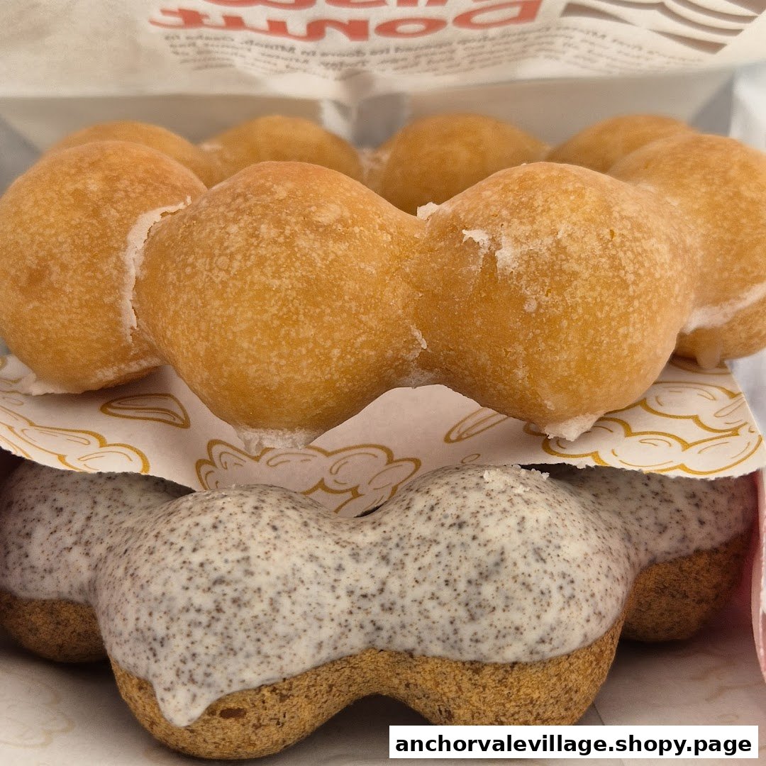 Close-up of two Mister Donut Pon de Ring donuts, one plain sugar and one cookies and cream, in a box.