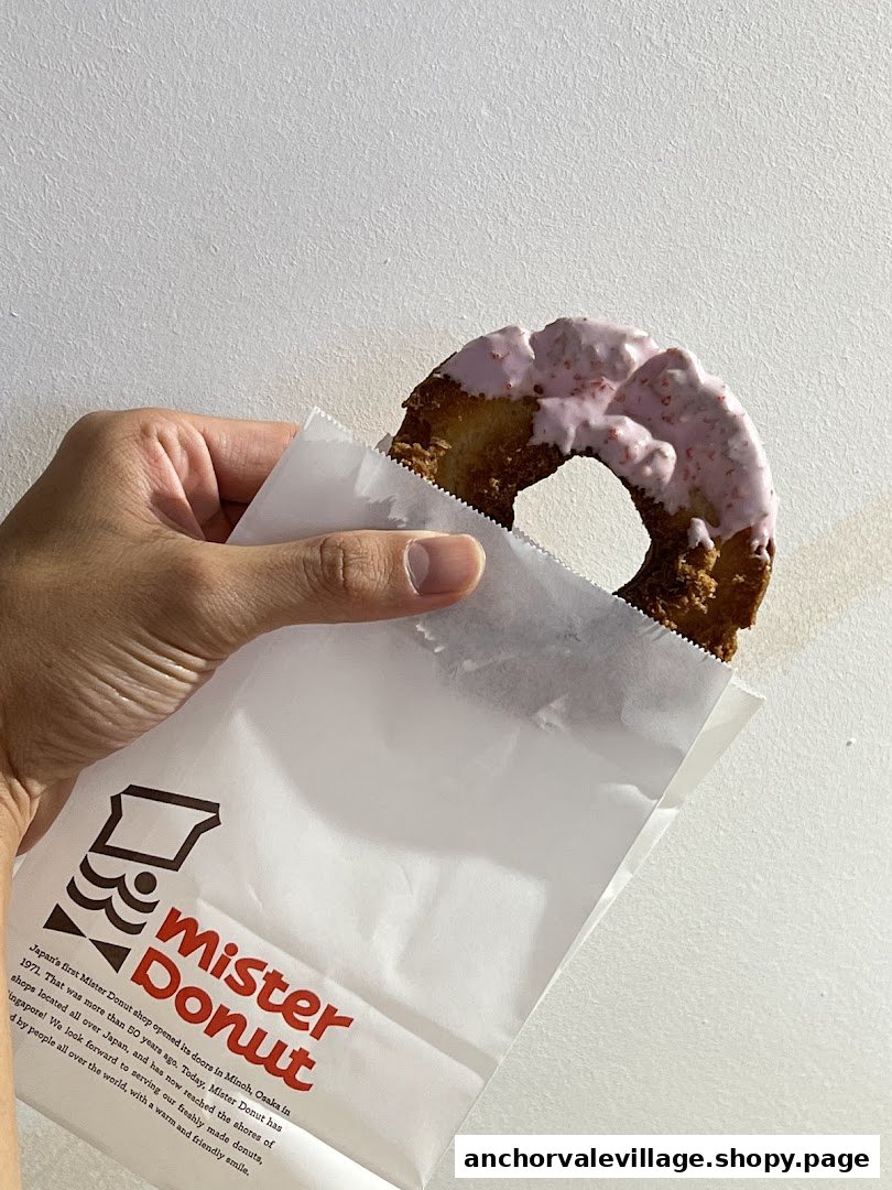 A hand holds a pink-frosted donut emerging from a Mister Donut branded paper bag.