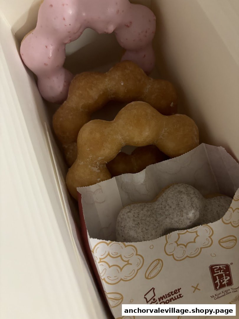 A box of colorful Mister Donut Pon de Ring donuts, including pink, plain, and speckled varieties.