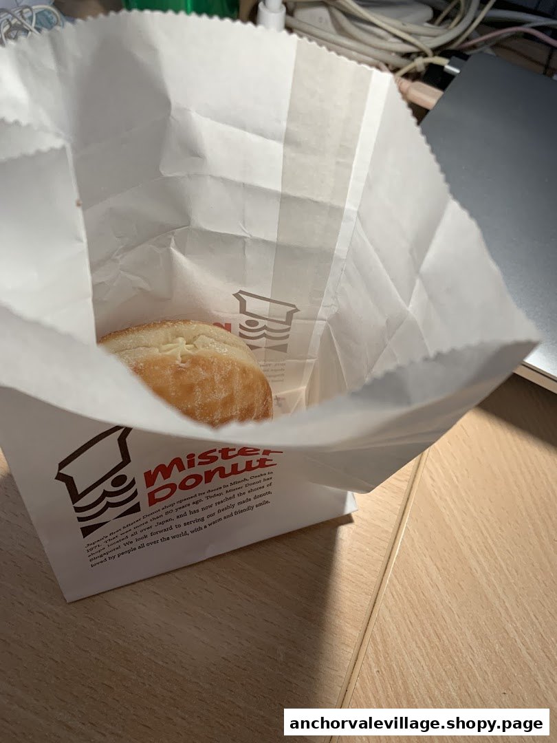 A freshly made donut peeks from a branded Mister Donut paper bag.