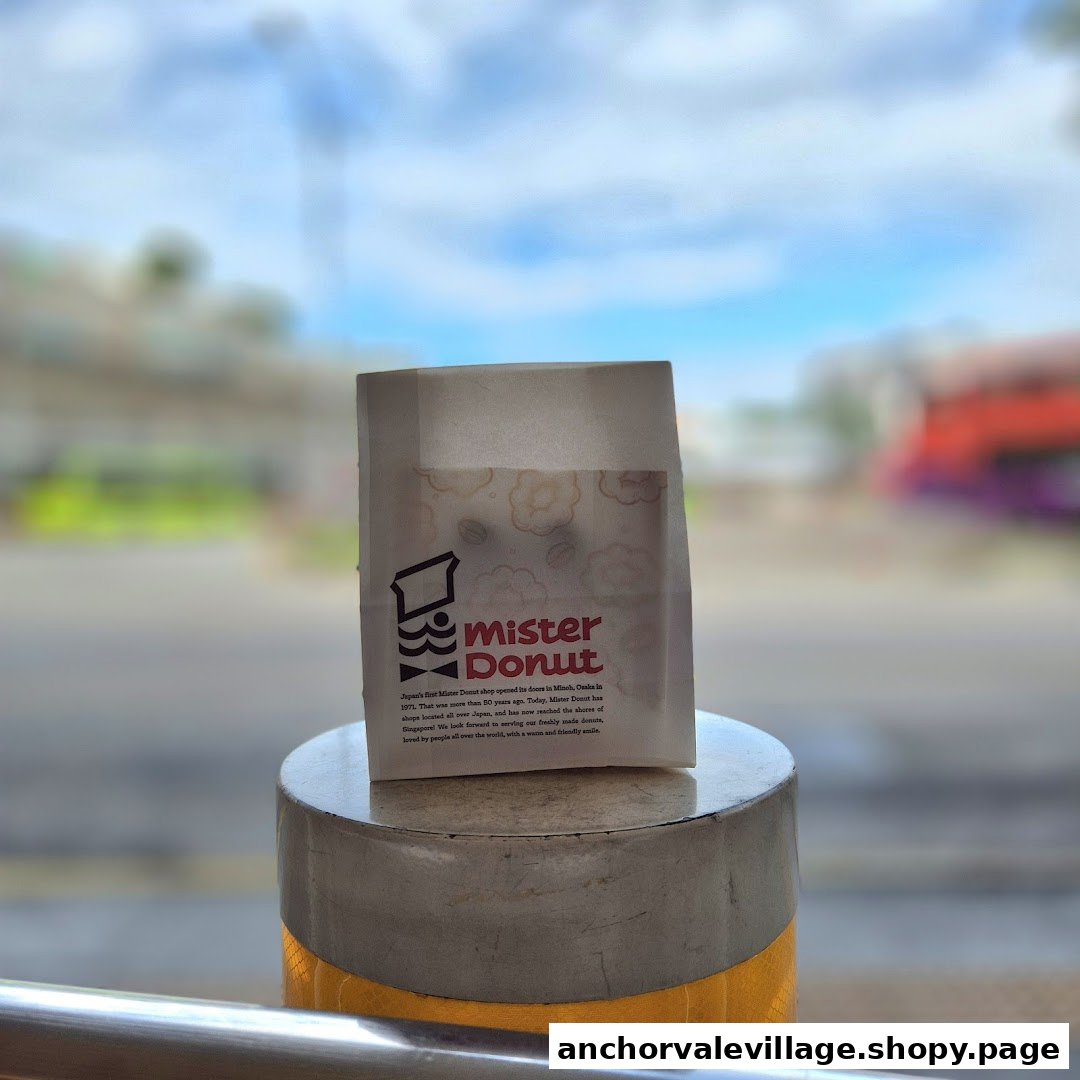 A Mister Donut branded paper bag, featuring its logo and a brief history, placed outdoors.