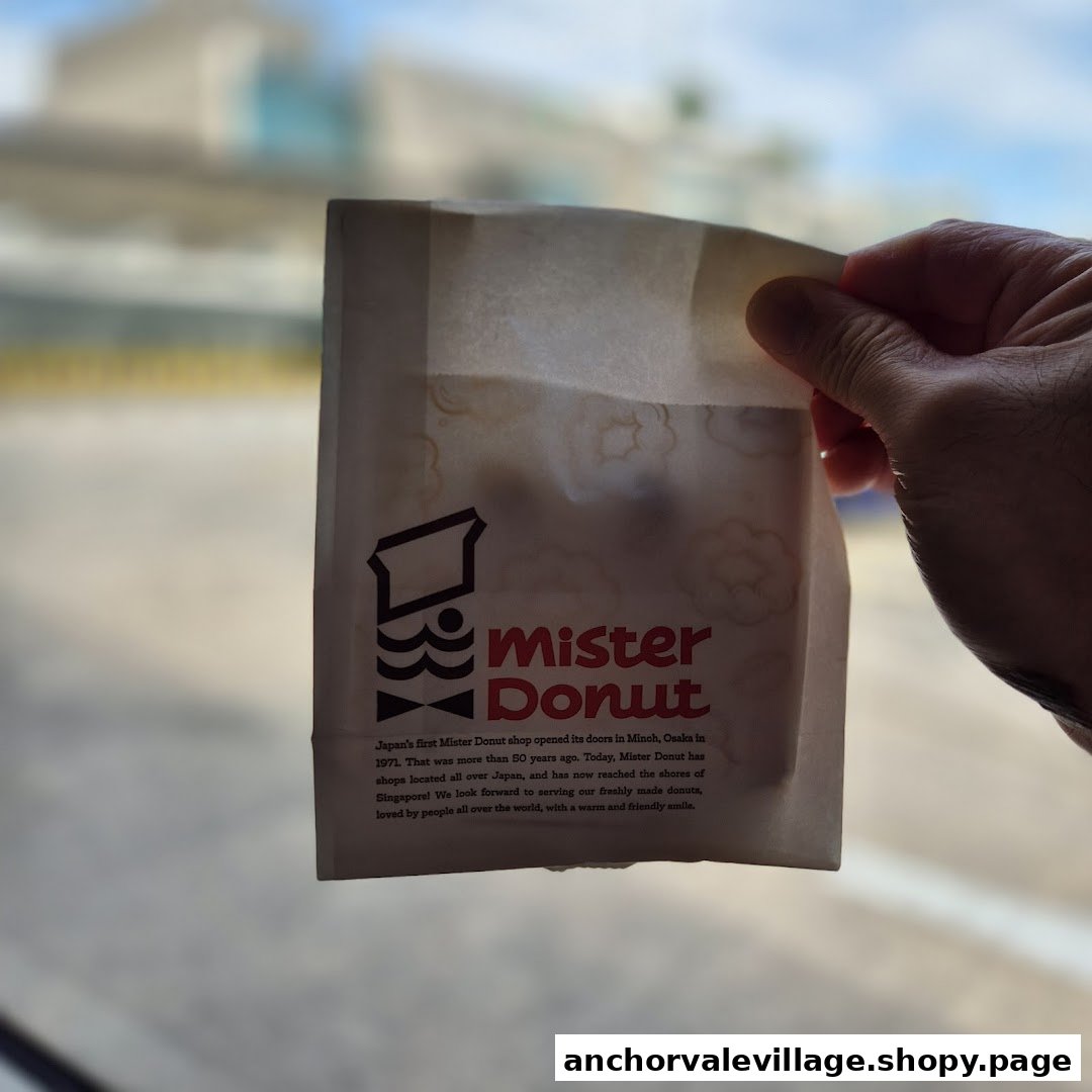 A hand holds a Mister Donut paper bag featuring the brand logo and history.
