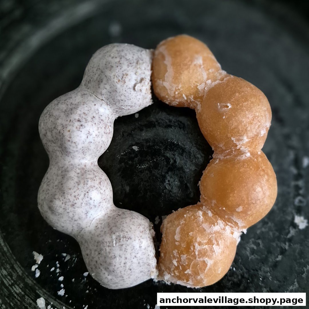 A close-up of a two-toned mochi donut, half glazed and half cookies and cream, on a dark surface.