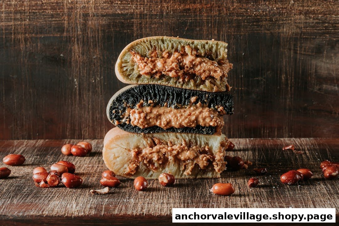 A stack of three colorful pancakes, filled with peanut butter, on a rustic wooden surface with scattered peanuts.
