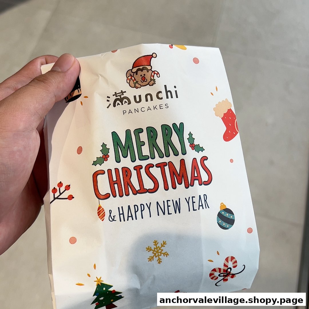 A hand holds a festive Munchi Pancakes paper bag adorned with Christmas greetings and holiday illustrations.
