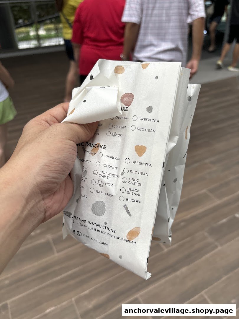 A hand holds a Munchi Pancakes bag displaying various pancake flavors and heating instructions.