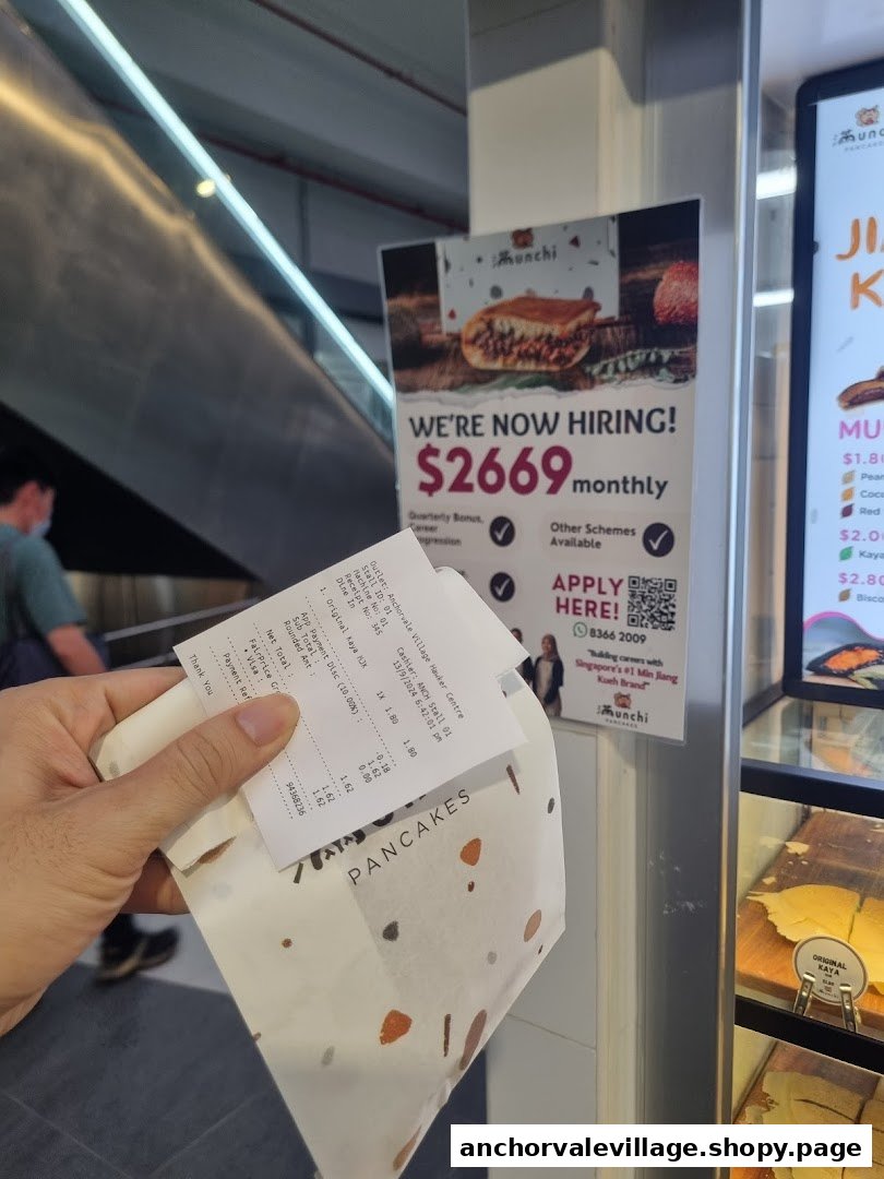 A hand holds a Munchi Pancakes receipt and packaging near a hiring poster and partial menu board.