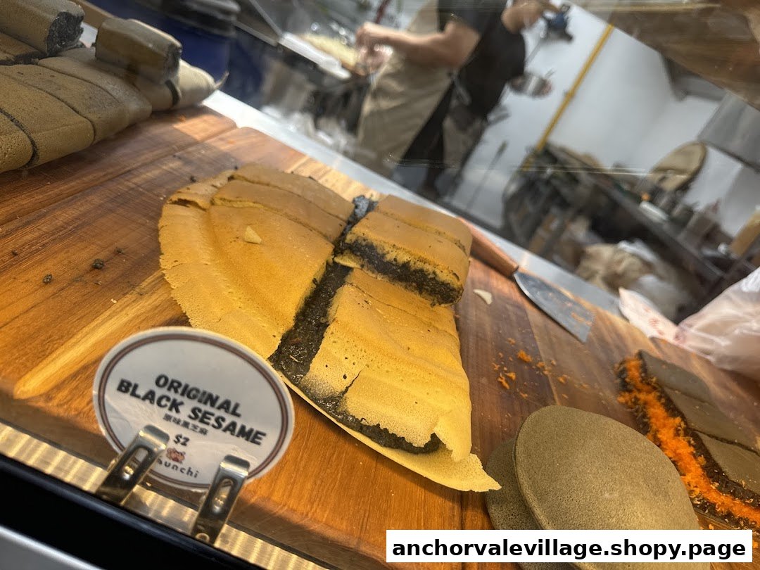 A large black sesame pancake, cut into pieces, displayed on a wooden board with a price tag.