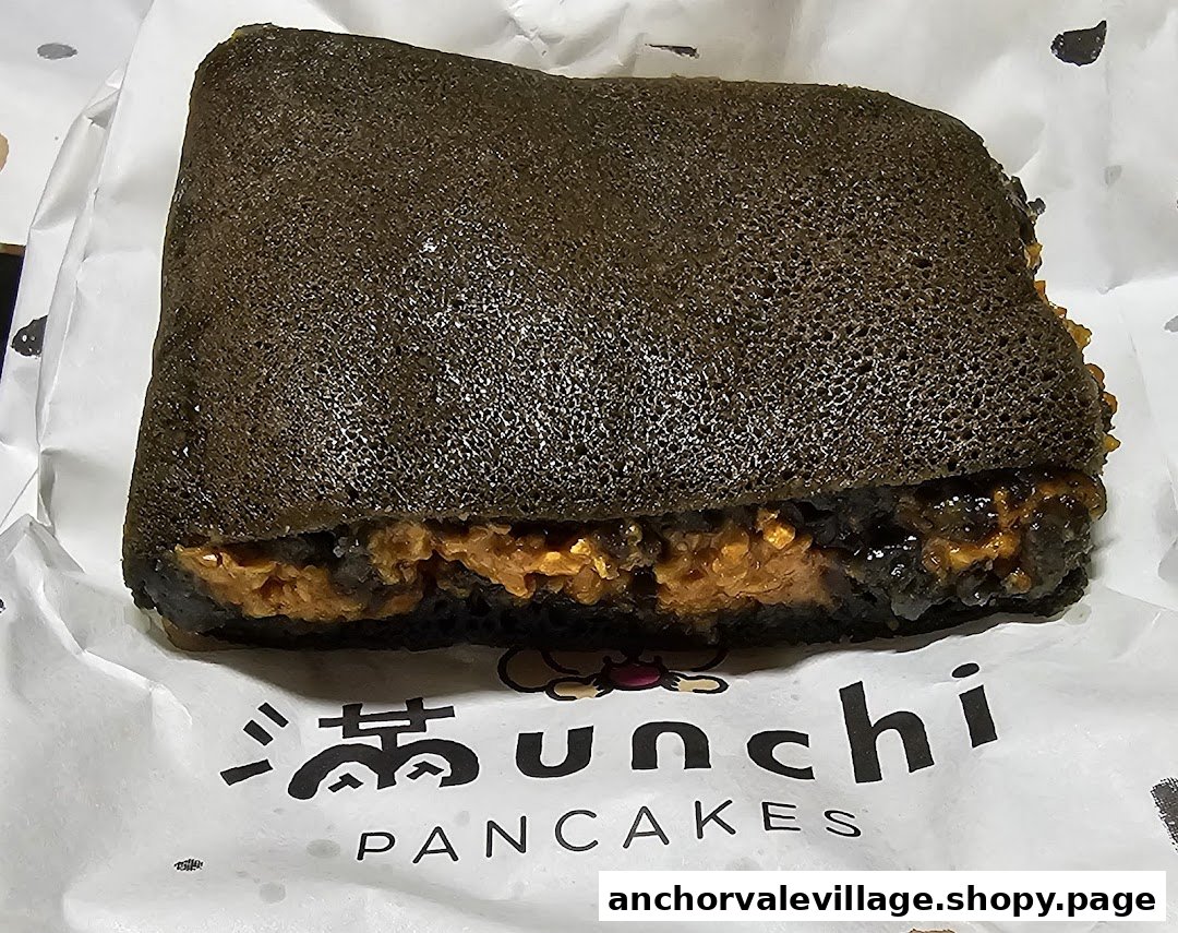 A dark-colored pancake filled with orange filling, wrapped in Munchi Pancakes branded paper.