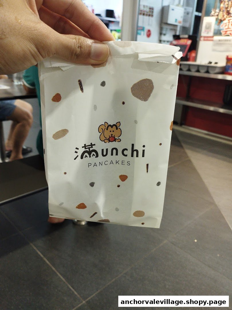 A hand holds a white paper bag with the "Munchi Pancakes" logo and squirrel mascot.