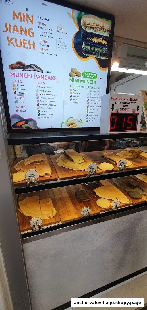A digital menu board displaying various pancake and kueh options with prices, alongside a display case of prepared items.