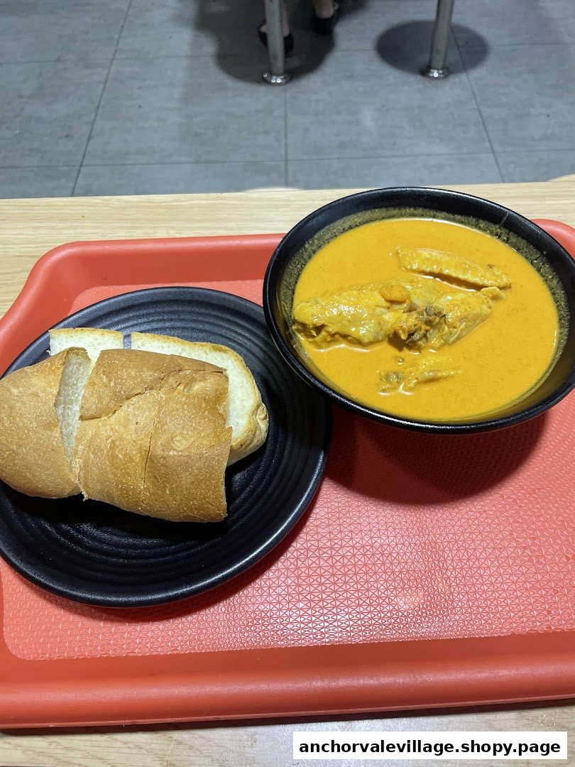 A bowl of rich yellow chicken curry with sliced bread on a red tray.