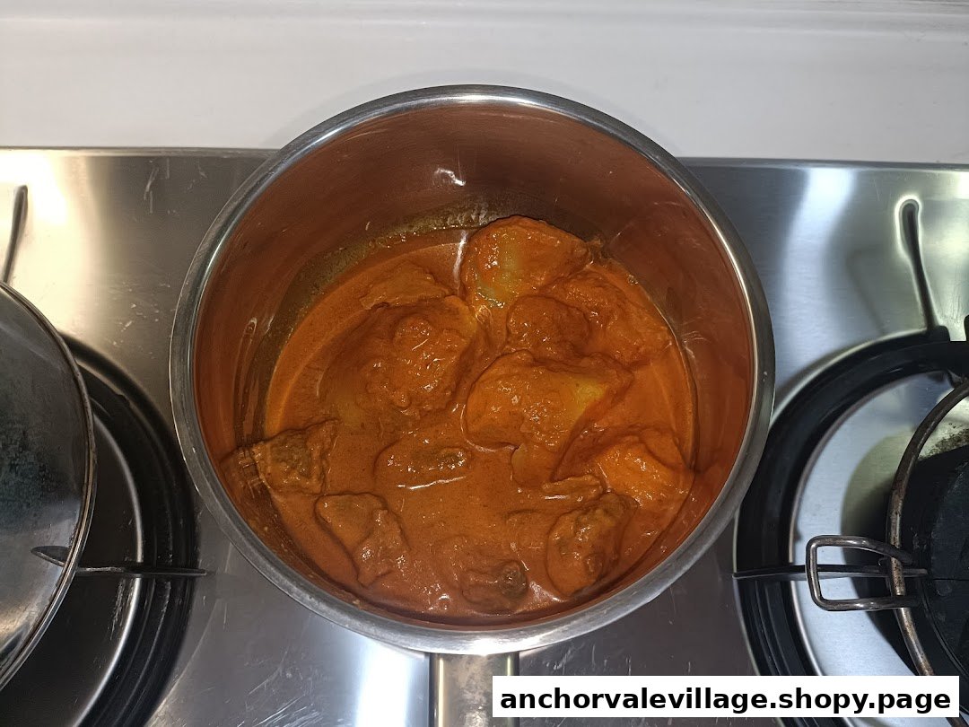 A pot of rich, orange Nanyang Curry chicken simmering on a stove.