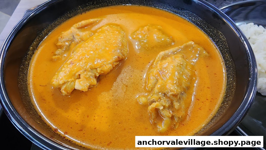 A close-up of a rich, orange chicken curry in a black bowl, with white rice visible.