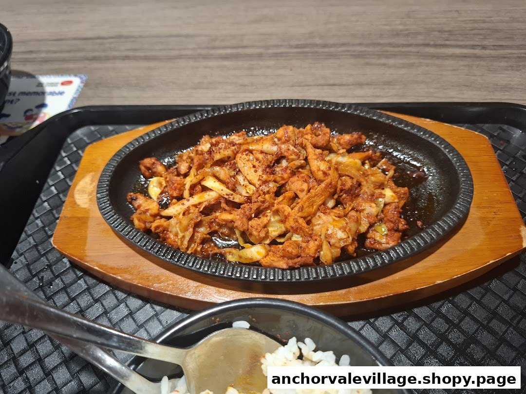 A close-up of a sizzling plate of spicy stir-fried meat and vegetables, served with rice.