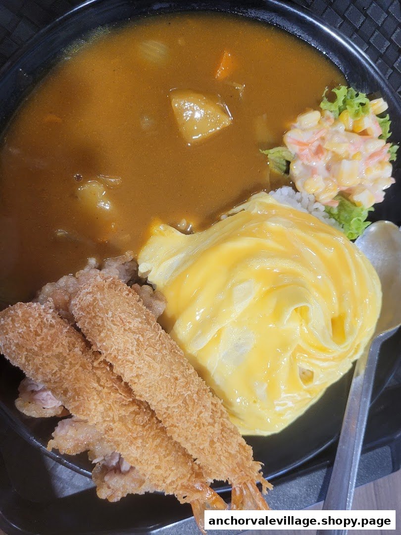 A delicious Japanese curry dish with fluffy omelet rice, crispy fried shrimp, and fresh salad.