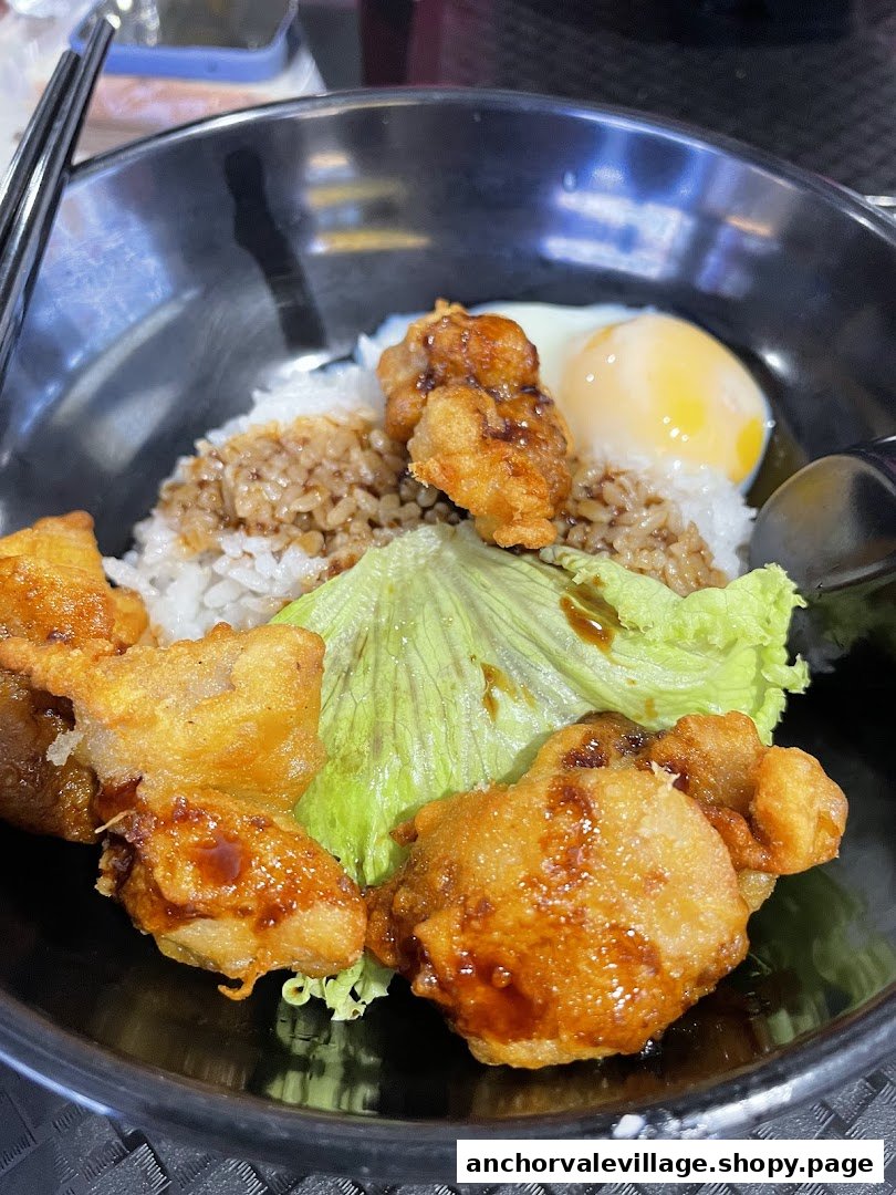 A close-up of a delicious Japanese donburi bowl with crispy fried chicken, rice, lettuce, and a soft-boiled egg.