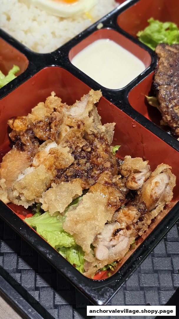 Close-up of crispy fried chicken with sauce and lettuce in a Japanese bento box.