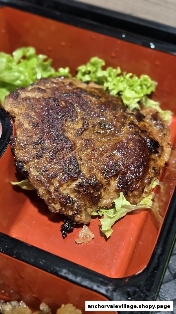 A close-up of a grilled meat patty served with fresh lettuce in a vibrant red bento box.