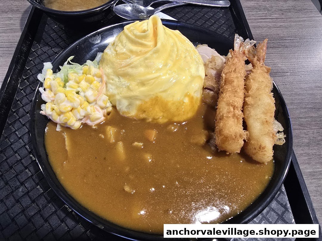 A close-up of a Japanese curry dish with omurice, fried shrimp, and corn salad on a black plate.