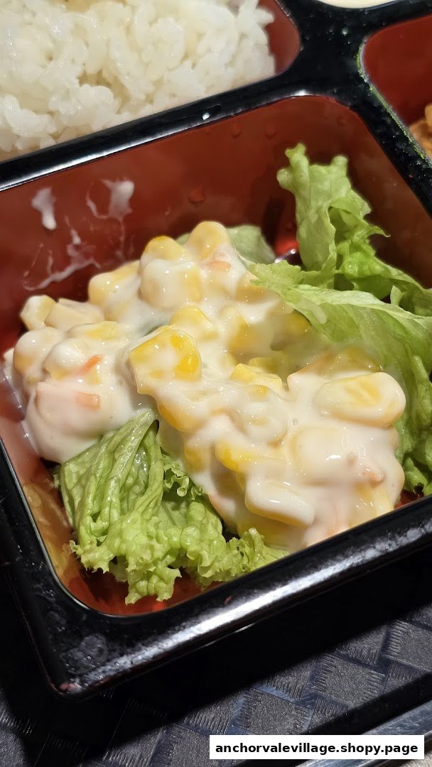 A close-up of a creamy corn salad with fresh lettuce, served in a red bento box compartment.