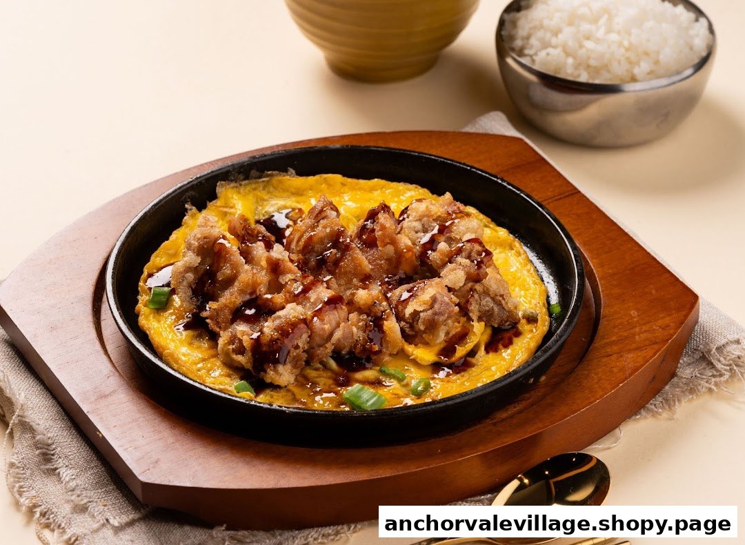 A sizzling plate of crispy fried chicken on fluffy egg, drizzled with sauce, served with rice.