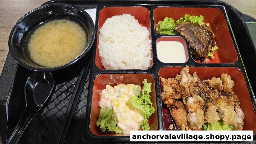 A Japanese bento box featuring rice, miso soup, grilled fish, fried chicken, and corn salad.