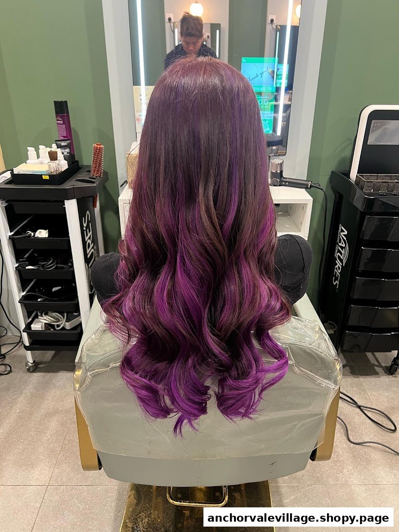 A person with vibrant purple and brown wavy hair, freshly styled, sitting in a modern hair salon.