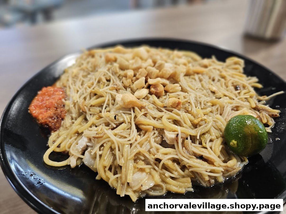 A close-up of a plate of Hokkien Mee with chili and a calamansi lime.